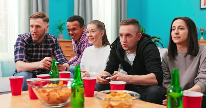 Group of friends play video games together at home, having fun. A smiling man competes with a friend in his favorite video game.