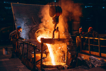 Pouring bright liquid iron or metal with sparks into container in steel mill or workshop blast furnace foundry. Metal casting process in metallurgical plant. - obrazy, fototapety, plakaty