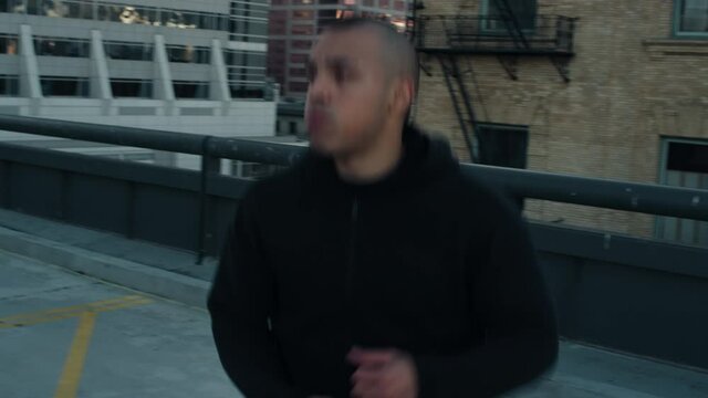 Latino athlete with a mohawk warms up on a city parking garage