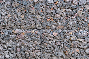 Stones and gravels in wire mesh background. Rockfall protection barrier. Gabion wall construction using wire mesh basket. Modern wall construction.