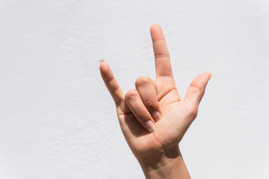 Closeup of the ILY hand sign against a white wall background
