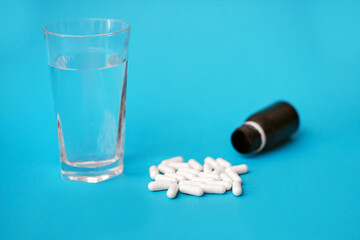 White pills and a glass of water on a blue background. Medical concept of medicines or vitamins for every day. Antibiotics are an irreplaceable aid in medicine