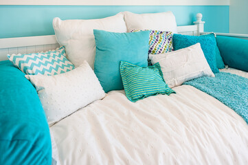 Close up of a bright and airy white poster bed with lots of aqua blue colored pillows.