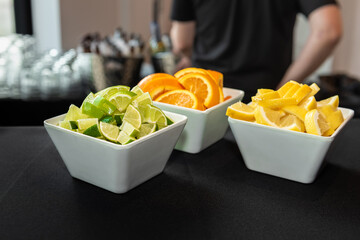 Containers of lime, orange and citrus garnishes on a bar top ready to be added to cocktails.