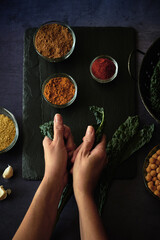 Two hands surrounded by spices rip kale leaves from their stem.