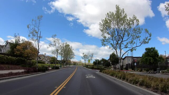 4K HD video driving point of view on newly paved access road between two neighborhoods. New houses on the left, older housing on the right. Cautions Signs for School Zone printed on the road.
