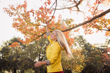 Young blonde woman in a yellow jacket having fun in the park. Standing. Autumn park background.