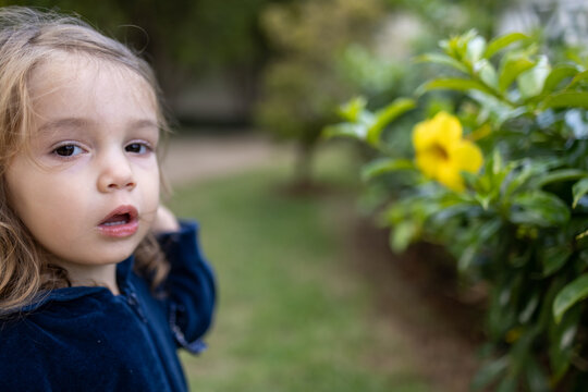 Criança menina loira brincando no jardim com uma flor amarela