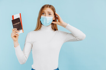 Shocked frightened young woman, in medical mask, holding passport with tickets