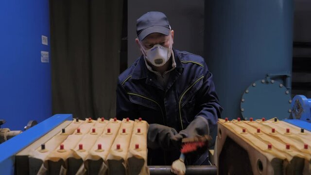 Production Process. Worker in a Respirator is Holding a Scraper and a Brush in his Hands. Moving one Filter Further. Intensely Brushing off the accumulated Dirt from two FIlters. Industrial Facility