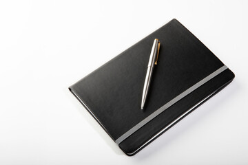 Silver ballpoint pen on black journal on white background.
