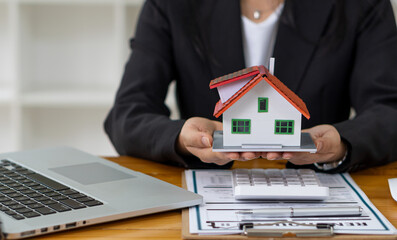 Real estate agent advising clients with contract documents and computers with front view house designs.