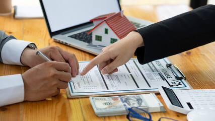 Real estate agent advising clients with contract documents and computers with front view house...