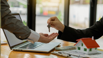Real estate agent advising clients with contract documents and computers with front view house...