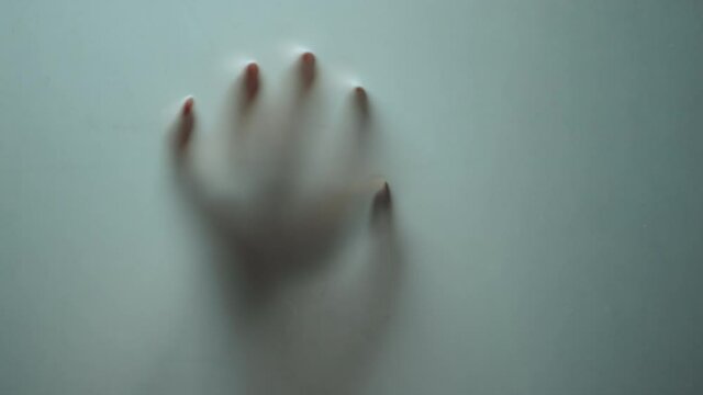 Macro female hand shadow sliding down on glass surface. Mystical horror.