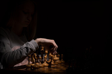 girl in the shadows plays vintage chess on a dark background. old chess. business concept