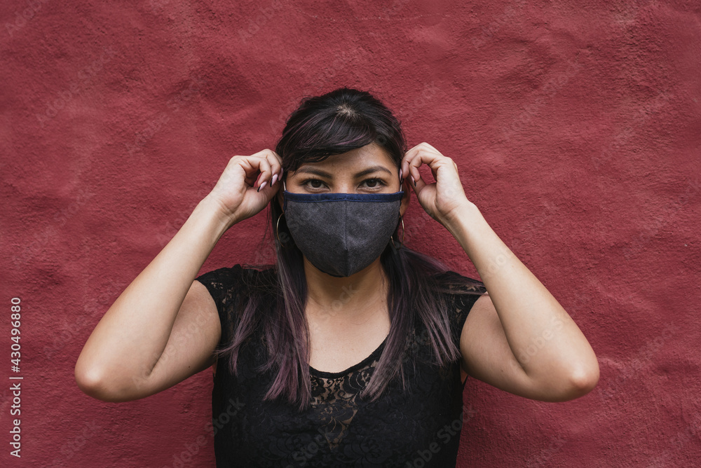 Wall mural young ecuadorian female wearing a fabric face mask on burgundy wall background