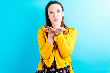 Beautiful adult young woman in yellow jacket on blue background blowing a kiss to the front. love...