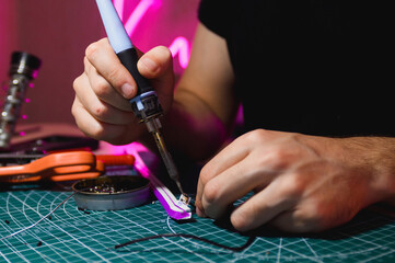 Cropped view of man soldering flex neon stripe near tools in workshop 
