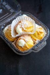 Cream puffs filled with pastry cream and sprinkled with powdered sugar in a transparent clear container.