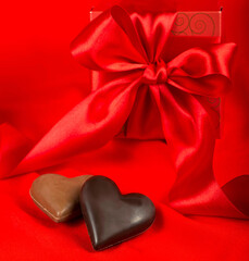 Chocolate hearts and gift box with ribbon on red silk background. black and milk chocolate.