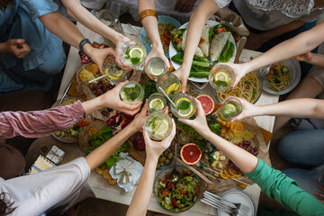 Top view closeup female friends hands cheers toasting glass of healthy beverage over serving table