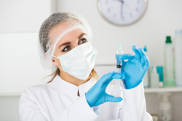 Fototapeta premium Smiling woman nurse preparing syringe for injection in hospital