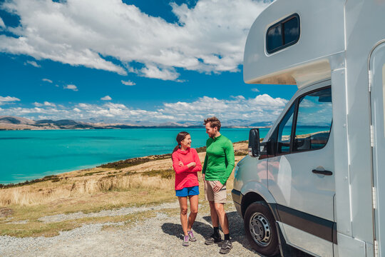RV motorhome camper van road trip on New Zealand. Young couple on travel vacation adventure. Two tourists looking at Lake Pukaki and mountains on pit stop next to their rental car