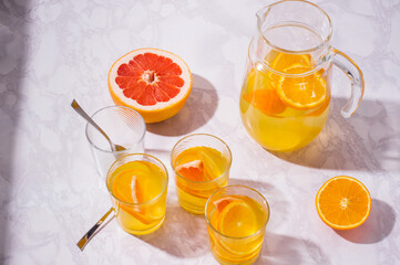 Lemonade pitcher with oranges, lemons and grapefruit on table. glasses of lemonade shot on white table