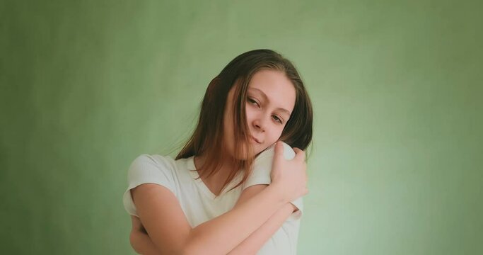 Cheerful young blonde woman in white t-shirt arms herself posing for camera at photo shoot by green wall closeup slow motion