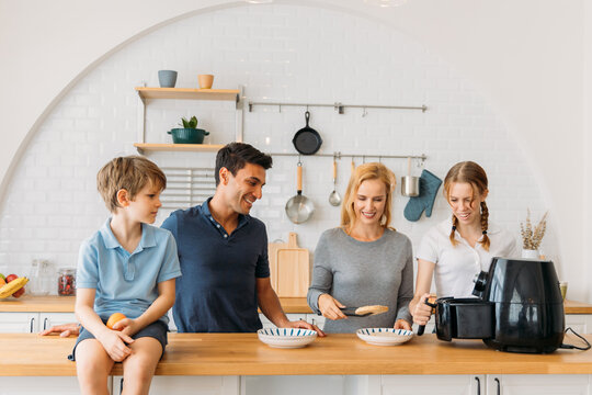 Cheerful caucasian handsome father and beautiful mother with son and daughter preparing healthy snacks in kitchen using air fryer at home