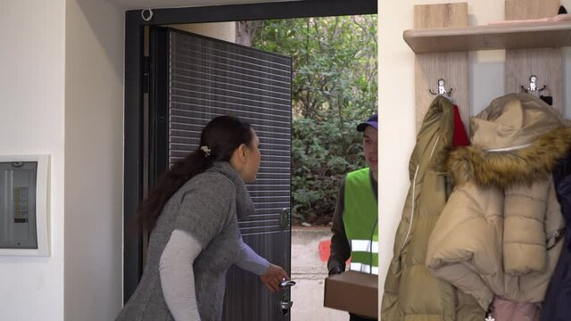 Latin american woman with a child receives a package from a courier on her doorstep. Online shopping, home delivery