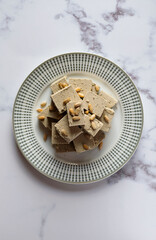 In the center of the frame are pieces of halva in a plate on a light marble table. Top view, vertical orientation.