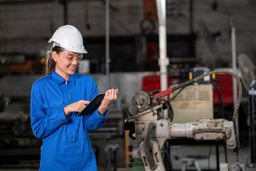 Engineer woman use tablet to control welding robotic automatic arm machine in the smart factory and smile. Automation manufacturing process for industrial 4.0. Technology, software and safety control