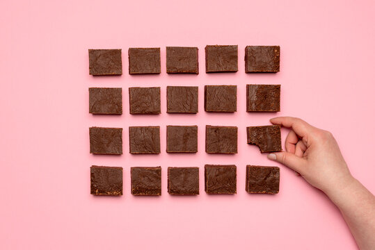 Woman hand grabbing a piece of fudge. Chocolate fudge on pink background top view.