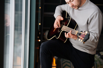 Handsome middle aged man playing guitar in a bedroom next to a window