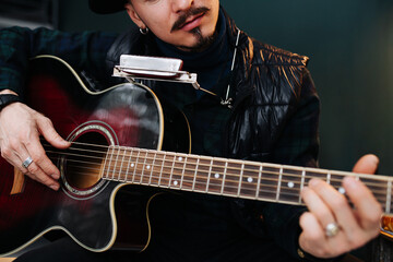 Obraz premium Close up image of middle aged man in a hat sitting on a stool, plaing guitar.