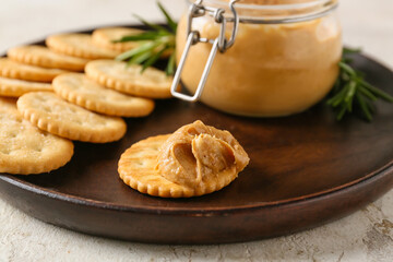 Plate with tasty crackers and jar with peanut butter on light background