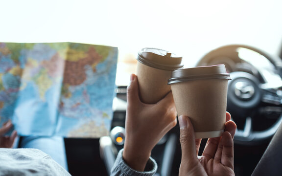 Closeup image of a couple traveler holding a map and clinking coffee cup together while riding in the car