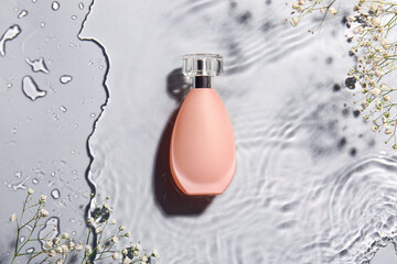 Bottle of perfume and flowers in water on grey background