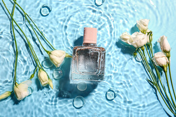 Bottle of perfume and flowers in water on color background