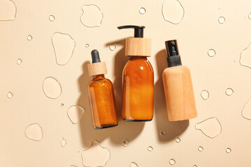 Bottles of cosmetic products on color background with water drops
