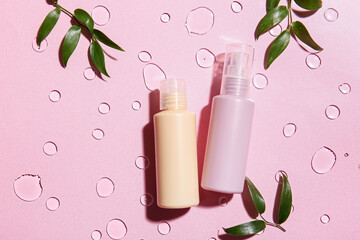 Bottles of cosmetic products and green leaves on color background with water drops