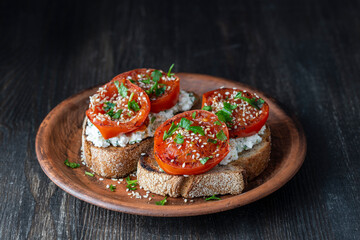 Delicious toasted bread with roasted red tomatoes, feta cheese, sesame seeds and herbs on plate
