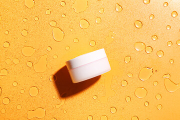 Jar of cosmetic product on color background with water drops