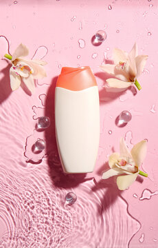 Bottle of cosmetic product and flowers in water on color background