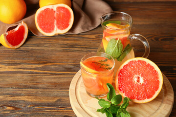Glass and jug of tasty grapefruit lemonade on wooden background