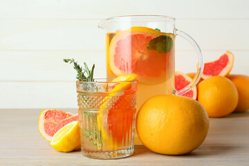 Glass and jug of tasty grapefruit lemonade on light wooden background
