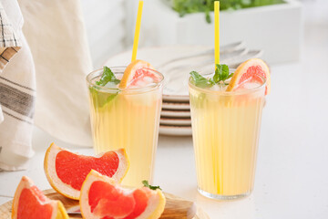 Glasses of tasty grapefruit lemonade on light background