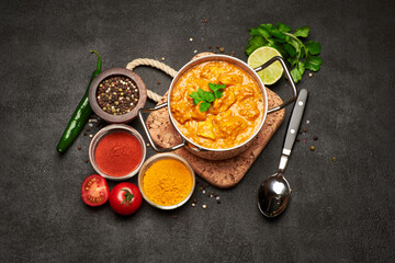 Pot of Traditional Chicken Curry and spices on cork serving board